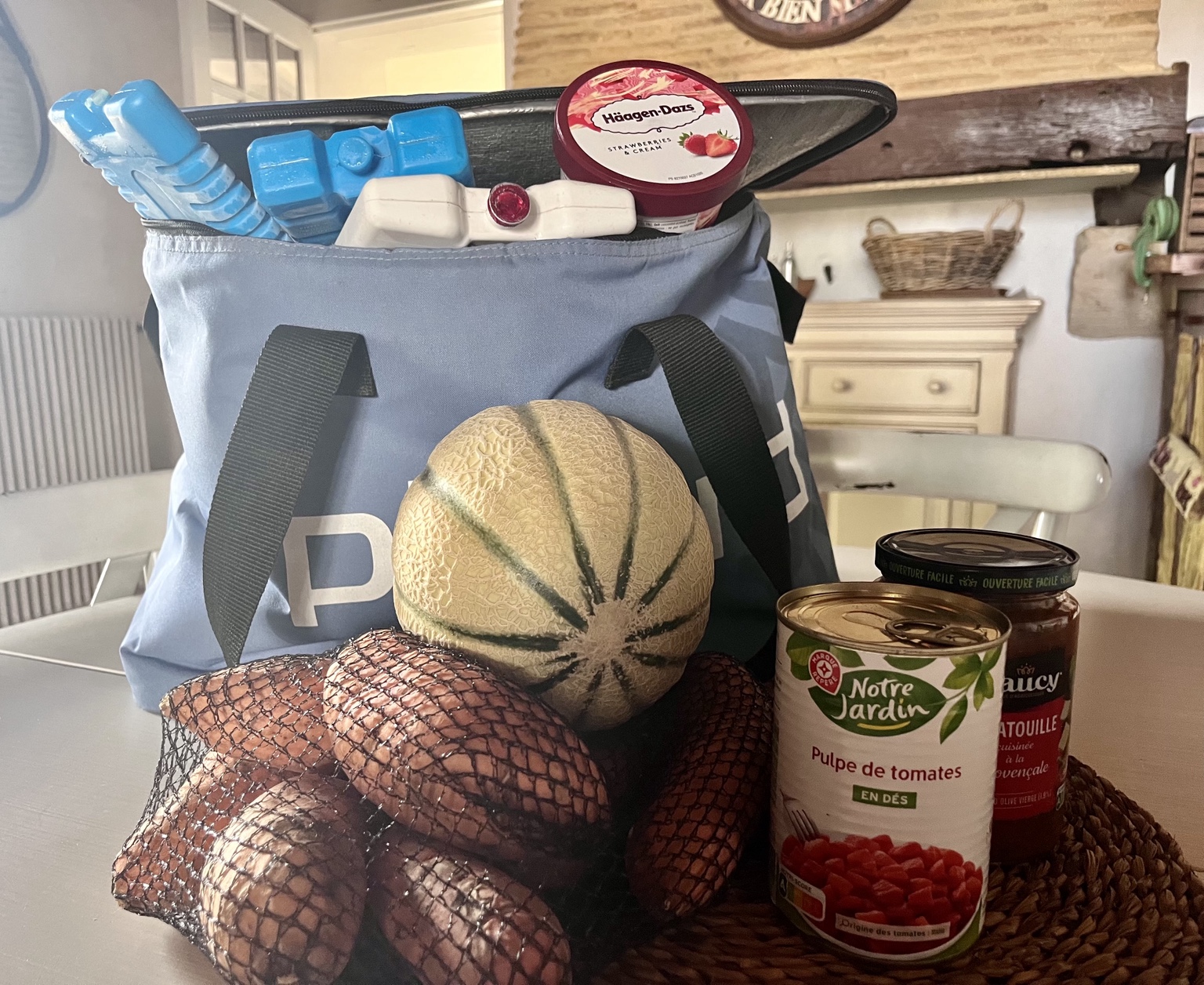 A French supermarket survival kit with a cold bag, freezer blocks, ice cream, potatoes, melon and tinned tomatoes