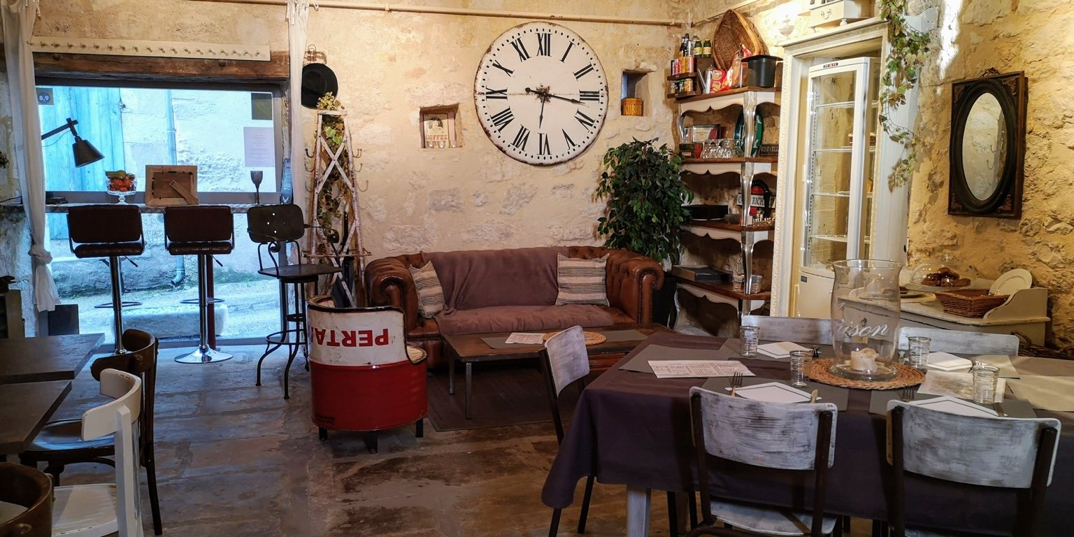 Empty tables laid for service in a rustic French stone restaurant beneath a very large wall clock